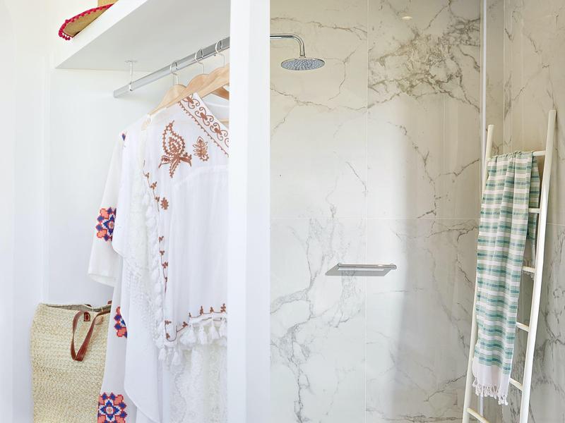 Heldere douche met marmeren tegels, handdoek aan een ladder en geborduurde jurk aan kledinghangers.