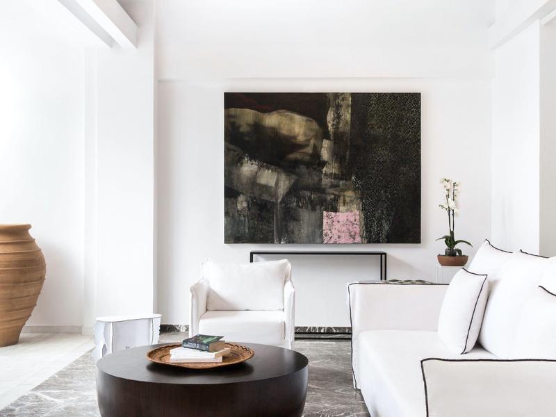 Moderne woonkamer met witte banken, bijzettafel en abstract kunstwerk aan witte muur.