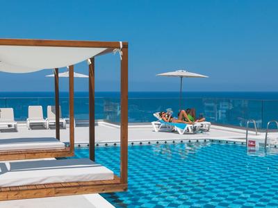 Area piscina moderna con lettini, lounge coperta e vista sul mare con cielo limpido.