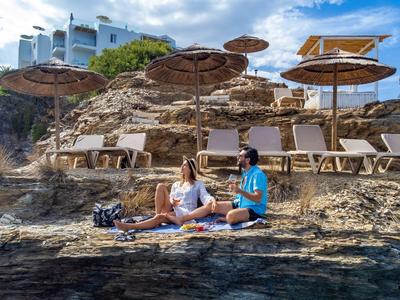 Due donne siedono su una roccia vicino al mare davanti ad aree rocciose per prendere il sole con ombrelloni.