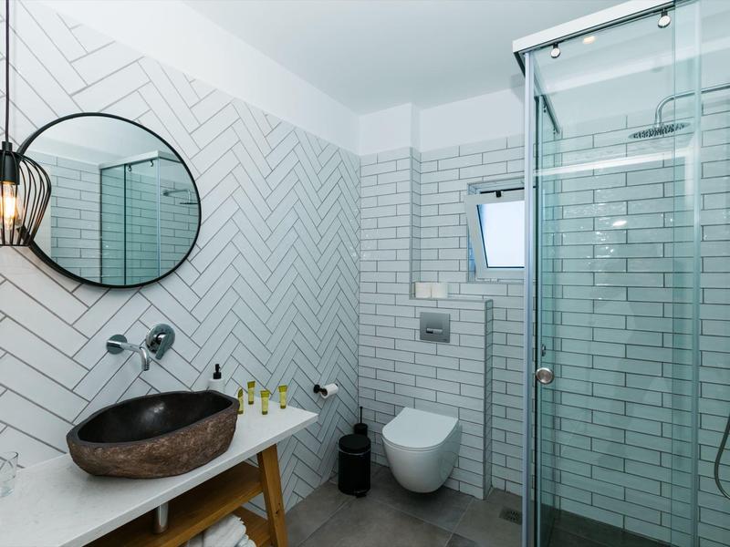 Bagno moderno con lavabo in pietra, specchio rotondo e cabina doccia con porta in vetro.
