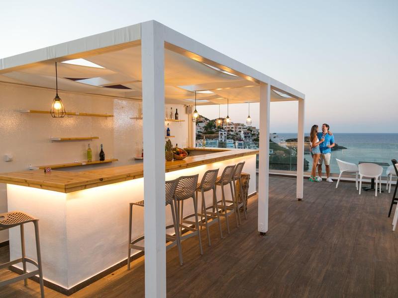 Bar esterna moderna con mobili in legno e vista sul mare al tramonto.