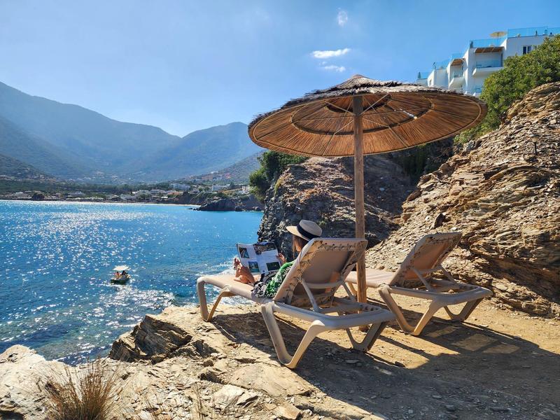 Due sdraio con un ombrellone su rocce vicino al mare con paesaggio montano.