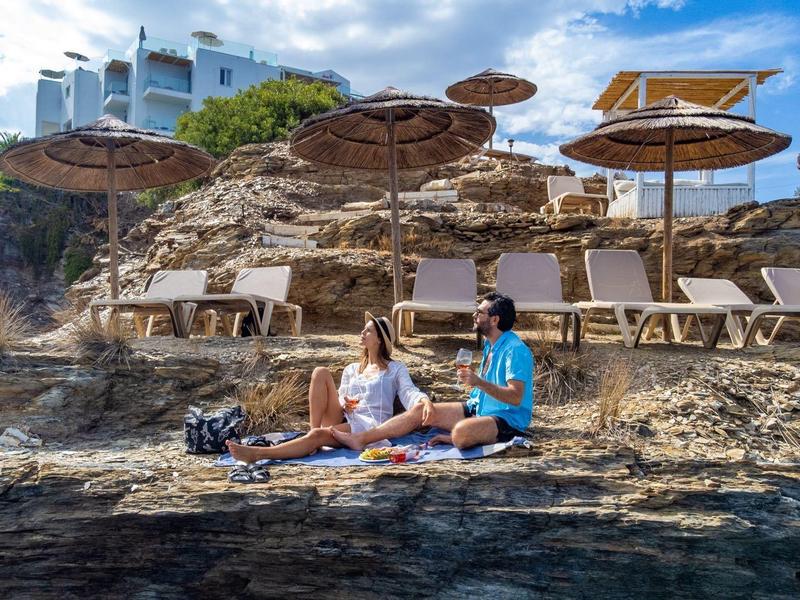 Due donne che si rilassano sulle rocce vicino al mare con sedie a sdraio e ombrelloni sullo sfondo.