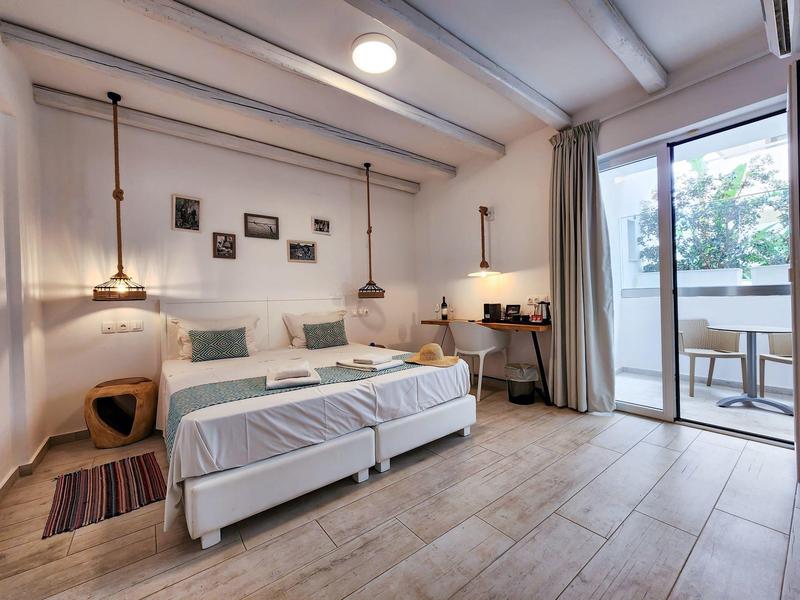 Camera d'hotel luminosa con letto matrimoniale, lampade sospese, scrivania e accesso al balcone con sedute.