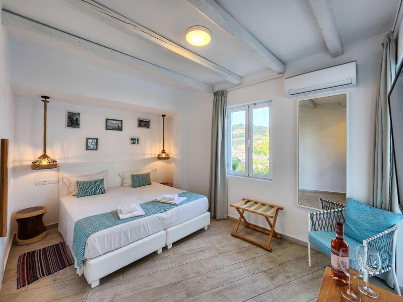 Camera d'hotel luminosa con letto matrimoniale, pareti bianche, soffitto con travi in legno e accesso al balcone