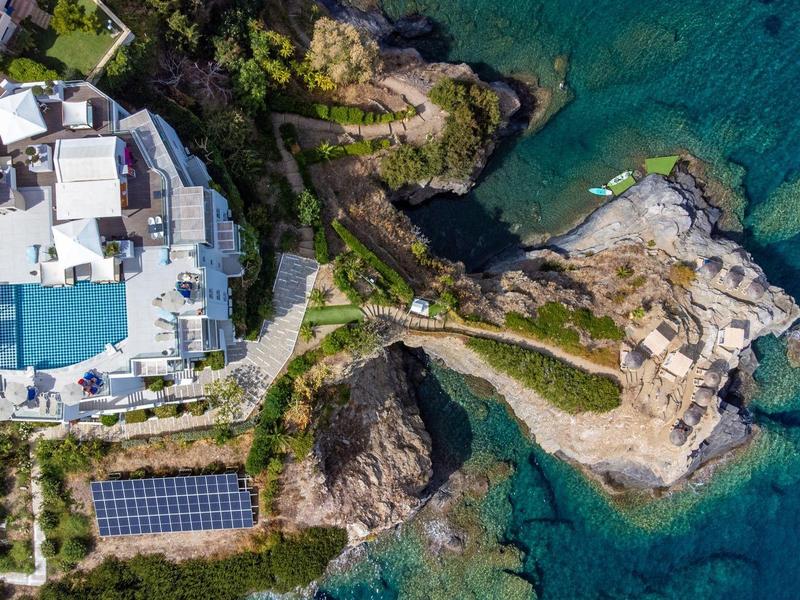 Veduta aerea di un hotel sulla costa con piscina, rocce e acqua limpida.