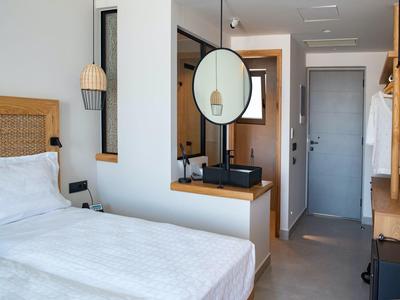 Modern hotelkamer met wit bed, houten accenten en open badkamer.