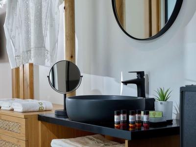 Moderne badkamer met een zwarte wasbak, ronde spiegel en houten meubels.