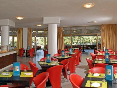 Modern restaurant met rode stoelen, geel servies, grote ramen en een lichte sfeer.