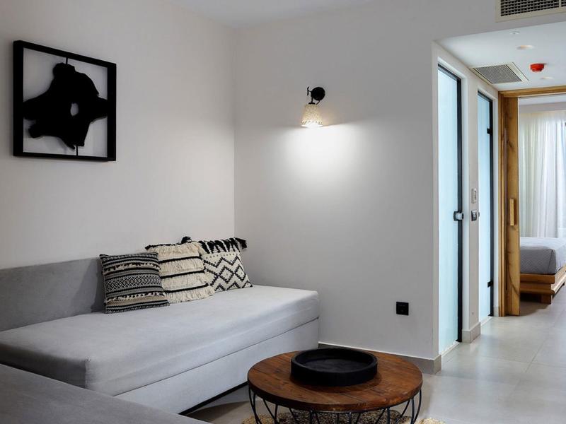 Moderne hotelkamer woonkamer met grijze bank, minimalistische kunst en ronde houten tafel.