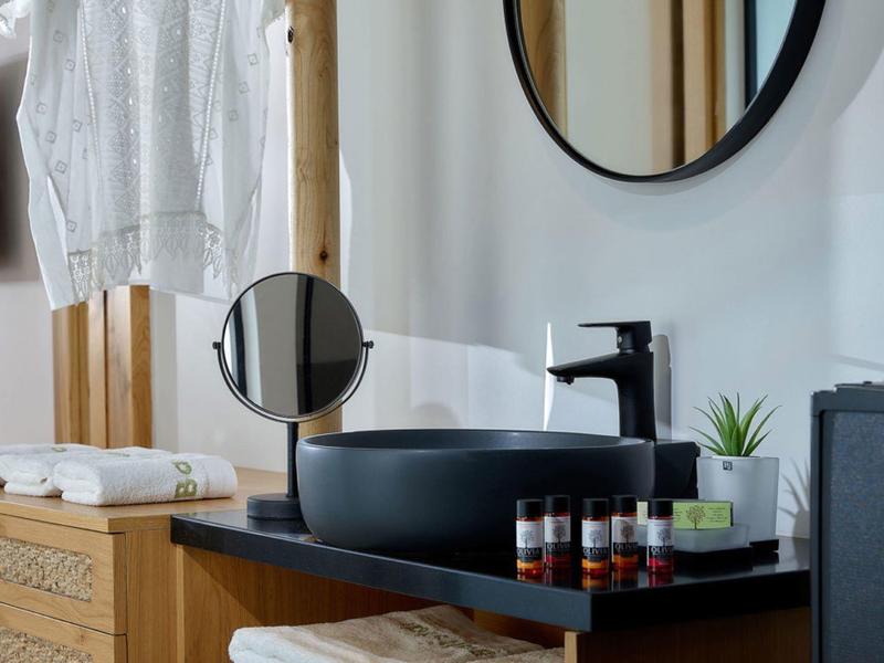 Moderne badkamer met een zwarte wasbak, ronde spiegel en houten meubels.