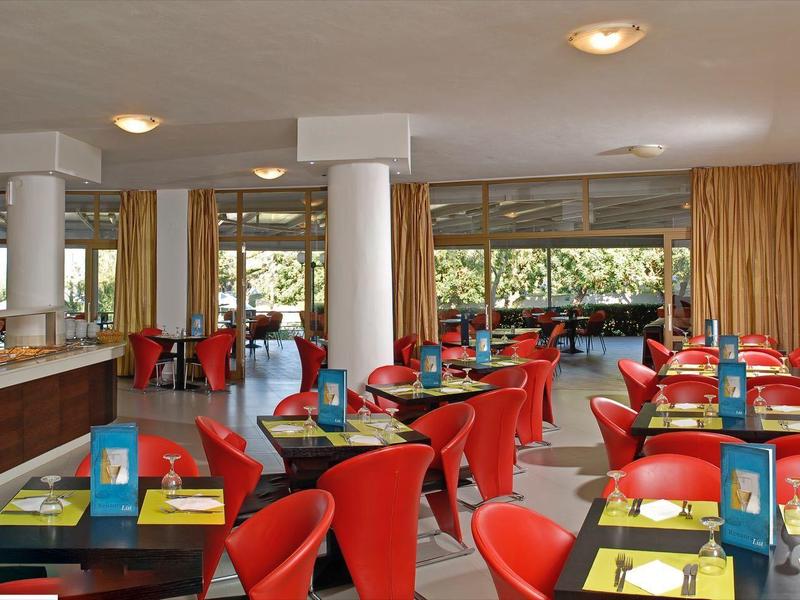 Modern restaurant met rode stoelen, geel servies, grote ramen en een lichte sfeer.