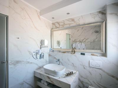 Moderne Badezimmer mit weißem Marmor, eckigem Waschbecken, großem Spiegel und eingebauten Deckenlampen.