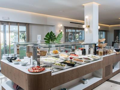 Buffet mit verschiedenen Speisen auf weißer Theke in modernem, hellem Frühstücksraum.