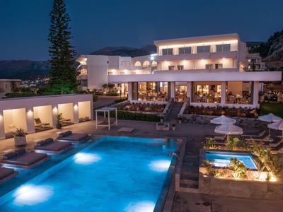 Hotel met verlichte zwembad, ligstoelen en jacuzzi bij schemering.