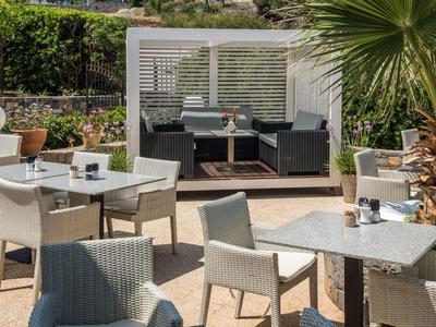 Moderne buitenruimte met tafels, stoelen en een loungehoek naast palmbomen.