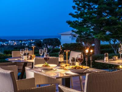 Abendessen im Freien auf Terrasse mit gedeckten Tischen, Kerzenlicht und Blick auf Stadt und Meer.