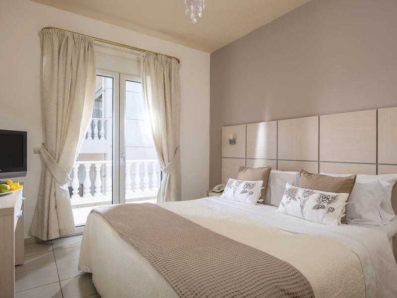 Schlichtes Schlafzimmer mit Doppelbett, hellen Vorhängen und Balkon hinter der Glastür.