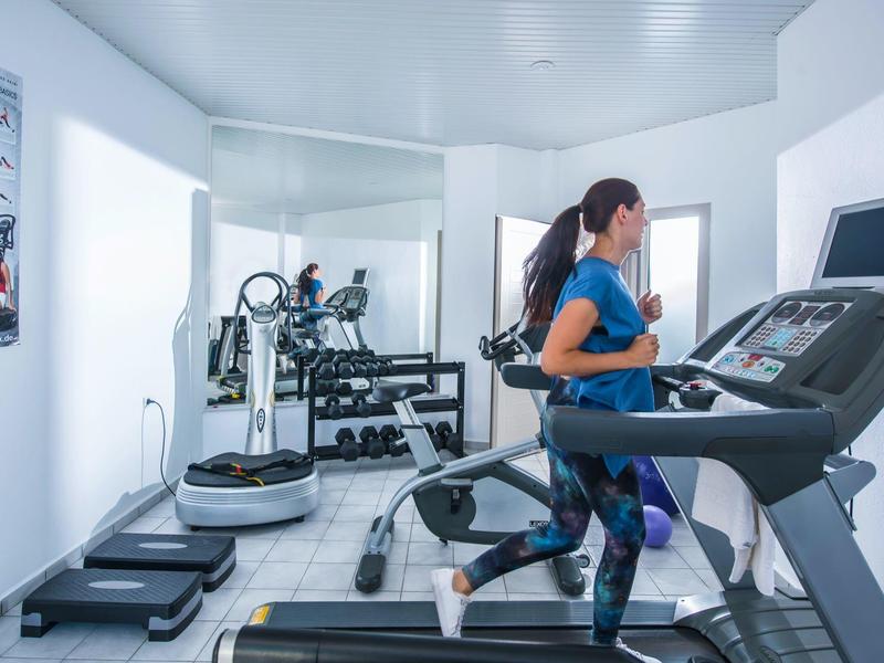 Frau läuft auf Laufband in hellem Fitnessraum mit Spiegel, Gewichten und Trainingsgeräten.