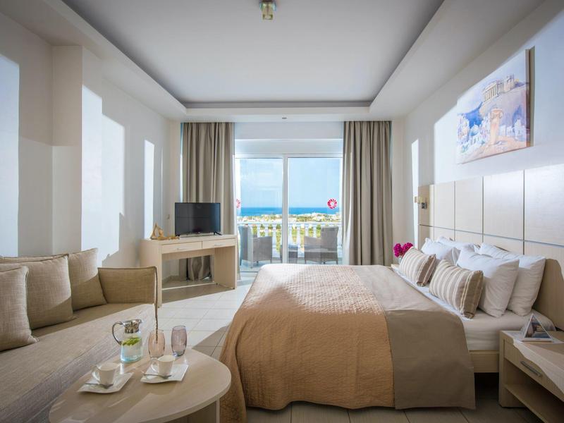 Modernes Schlafzimmer mit großem Bett, Sofa, Fernseher und Balkon mit Meerblick.