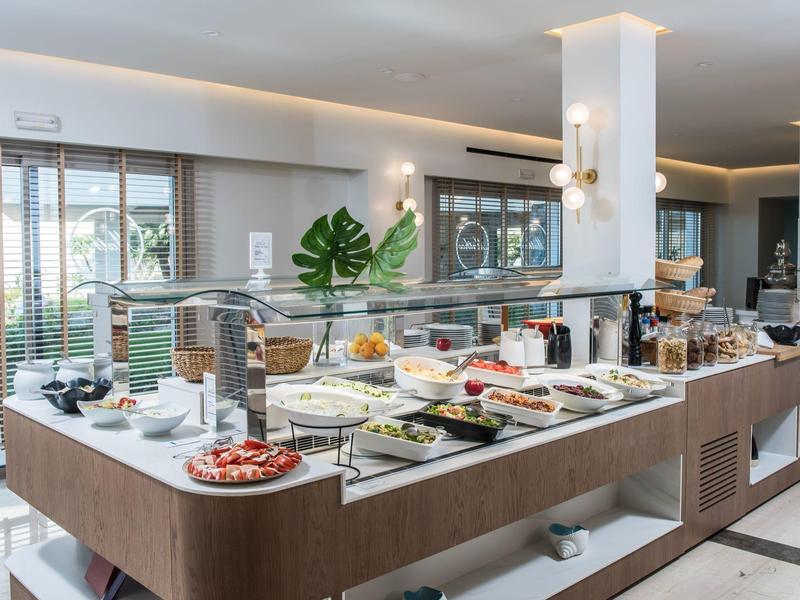 Buffet mit verschiedenen Speisen auf weißer Theke in modernem, hellem Frühstücksraum.