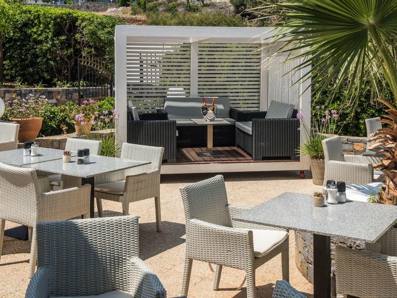 Moderner Außenbereich mit weißen Tischen, grauen Stühlen und einer überdachten Lounge-Ecke.