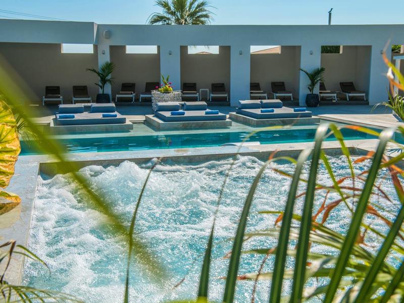 Moderner Pool mit eingebauten Whirlpools, Sonnenliegen und Pflanzen im Vordergrund.