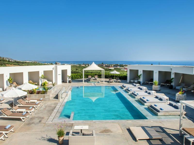 Moderner Außenpool mit Liegestühlen, weißer Pergola und Meerblick bei klarem Himmel.