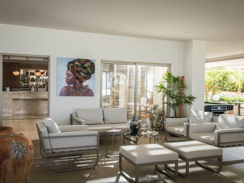 Helle Lounge mit weißen Sofas, Glastisch, grünem Pflanzenarrangement und Kunstbild an der Wand.