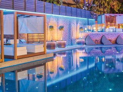 Moderní bazénová oblast s osvětlenými lehátky a kabinami v hotelu v noci.