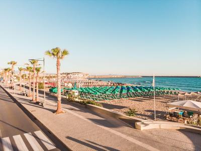 Pláž s zelenými slunečníky, palmami a chodníkem podél silnice za jasné oblohy.