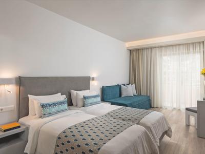 Camera d'hotel moderna con due letti, un divano letto e una grande finestra con tende.