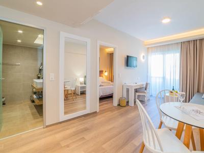 Prosvětlený hotelový pokoj s dřevěnou podlahou, balkonem a moderní koupelnou.