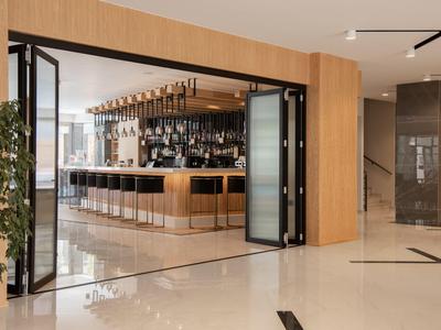Nowoczesny bar hotelowy z drewnianymi panelami, stołkami barowymi i szerokimi składanymi drzwiami.