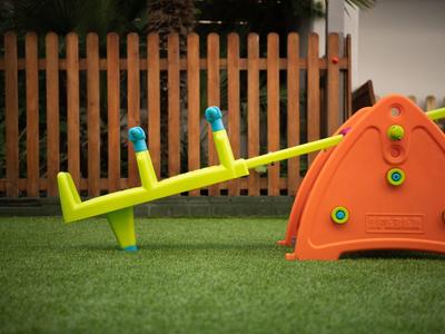 Barevná dětská houpačka na zelené trávě před dřevěným plotem.