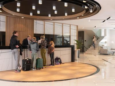 Recepce s hosty a zavazadly v moderní hotelové hale se schody v pozadí.