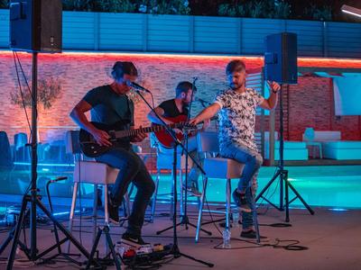 Tři hudebníci hrají živě na osvětleném venkovním pódiu.