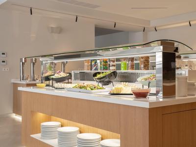 Bufet s saláty a talíři v moderní, světlé hotelové kuchyni.