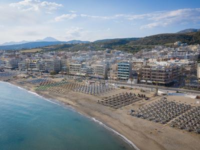 Letecký pohled na rušnou písečnou pláž s deštníky a městskou oblastí za ní.