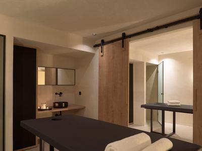 Moderní hotelový pokoj s tmavým masážním stolem a světlou koupelnou s posuvnými dveřmi