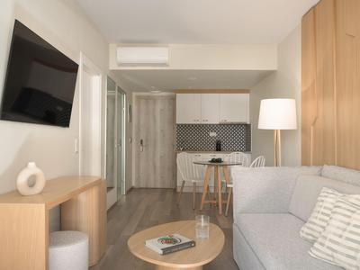Modernly furnished hotel room with kitchenette, sofa, dining table, and TV.