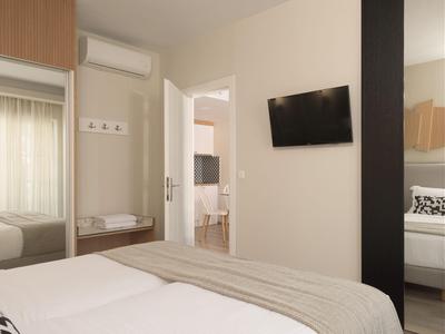 Modern hotel room with bed, wall-mounted TV, and view into adjoining bathroom.