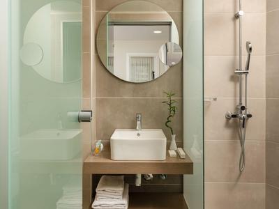 Modern hotel bathroom with sink, round mirror, and shower in neutral tones.