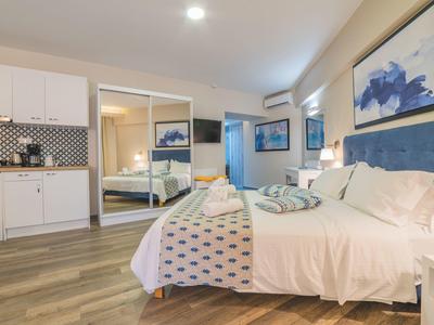 Moderní hotelový pokoj s manželskou postelí, zrcadlovou skříní a kuchyňským koutem.