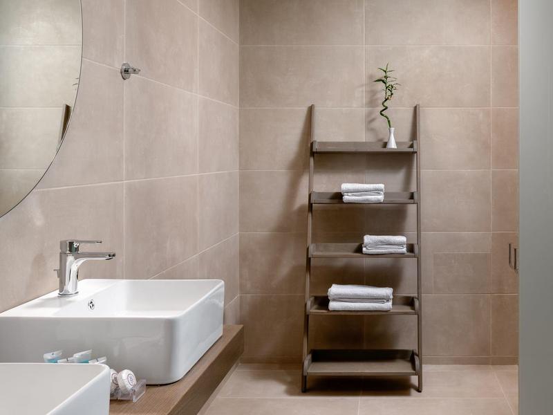 Moderní koupelna s obdélníkovým umyvadlem, dřevěnou policí a béžovou obklady.