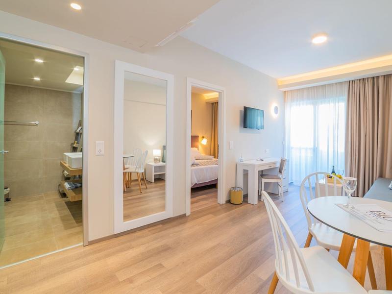 Prosvětlený hotelový pokoj s dřevěnou podlahou, balkonem a moderní koupelnou.