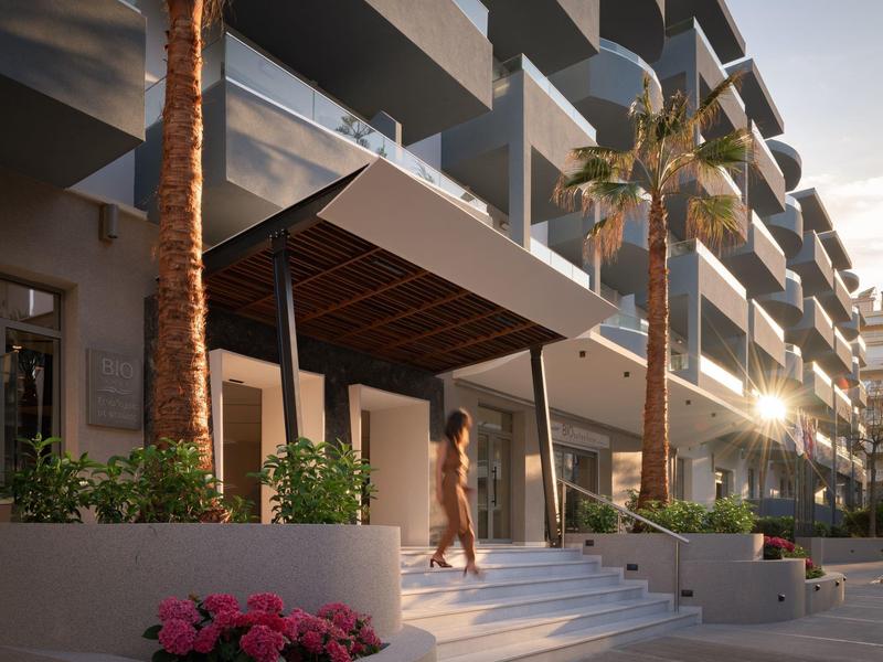 Hotelová budova s vchodem, palmami a schody při západu slunce.