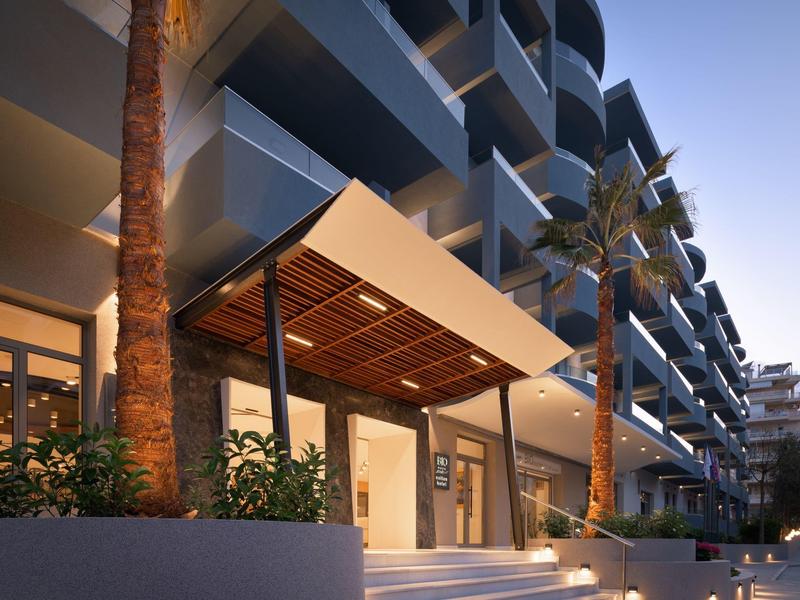 Moderní hotelový vchod s krytou stříškou a palmami za soumraku.