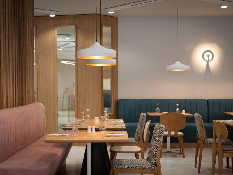 Moderní jídelna s dřevěnými stěnami, modrými lavicemi a různými židlemi u dřevěných stolů.